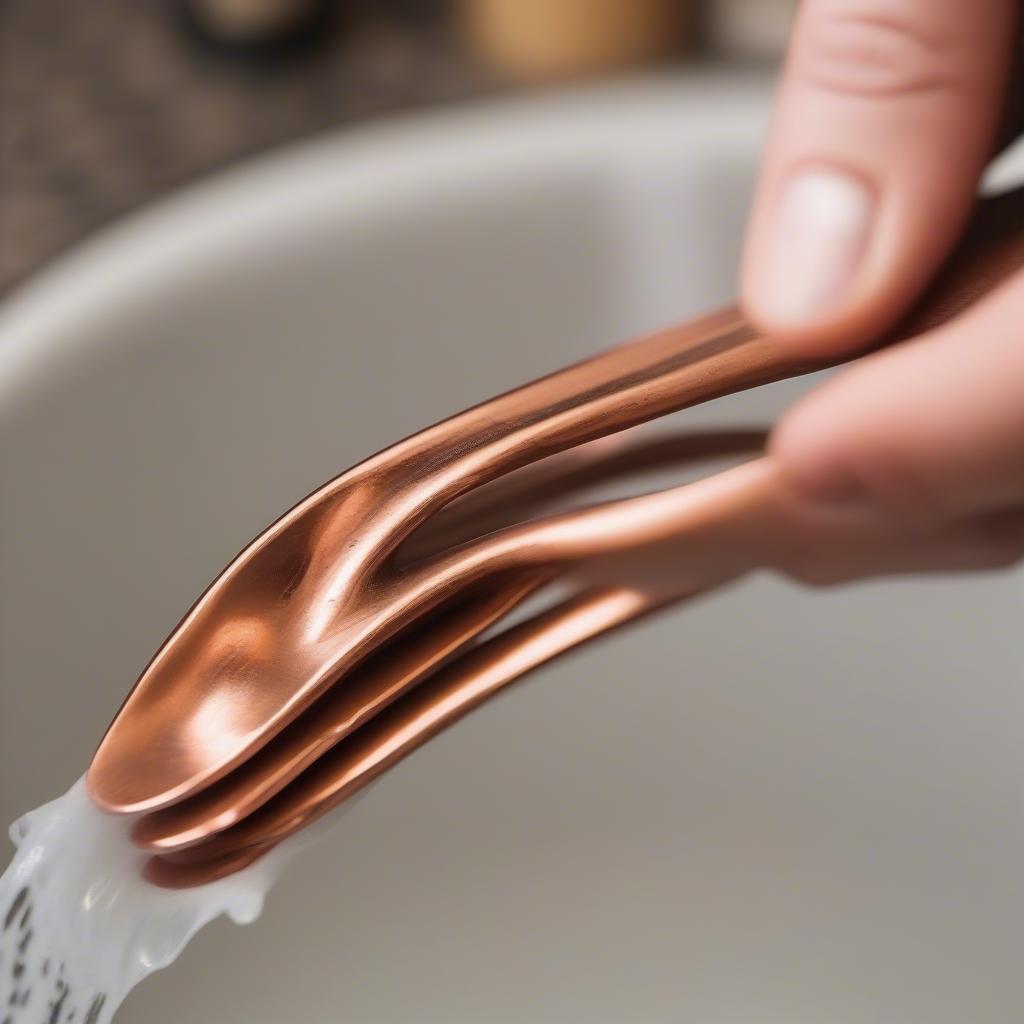 A person carefully hand washes hammered copper flatware with gentle soap and a soft cloth, demonstrating proper care techniques.