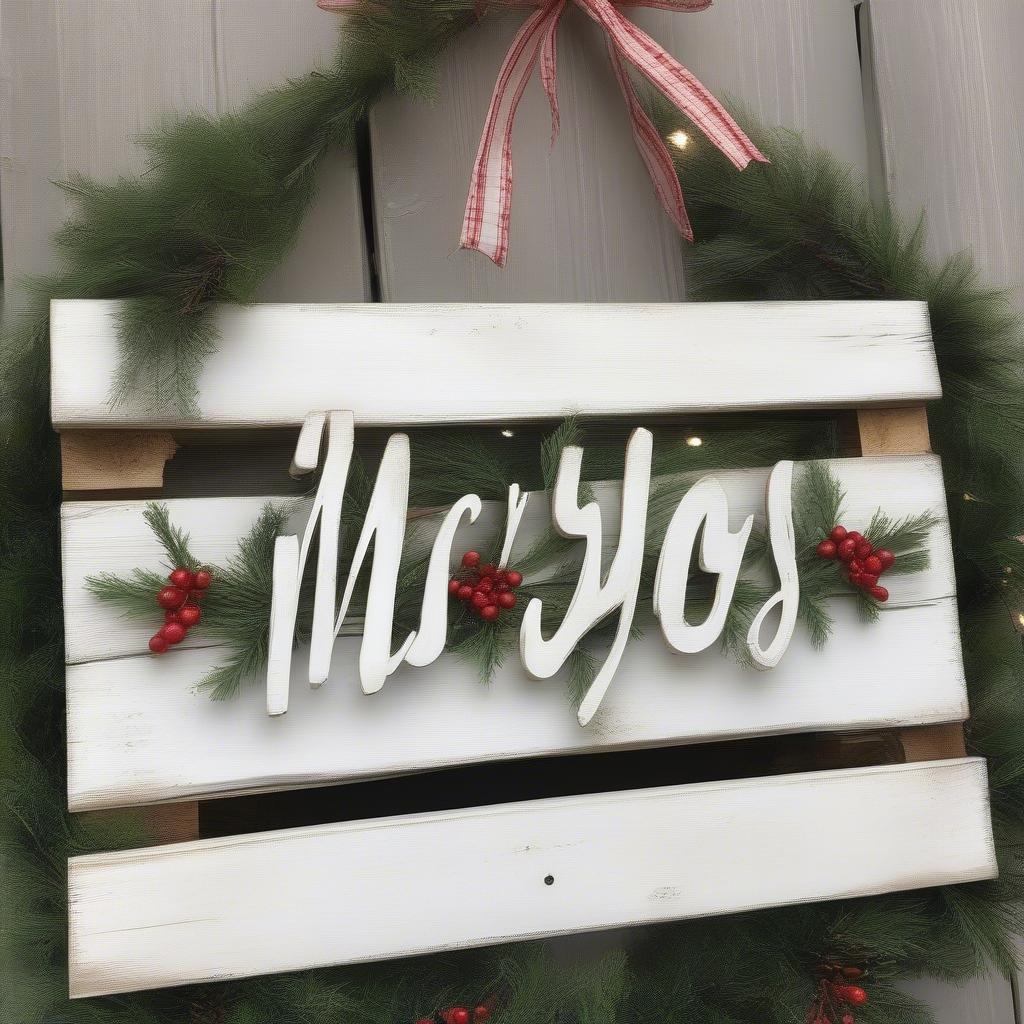 A DIY "Merry Christmas" sign made from reclaimed pallet wood, painted white and decorated with greenery.