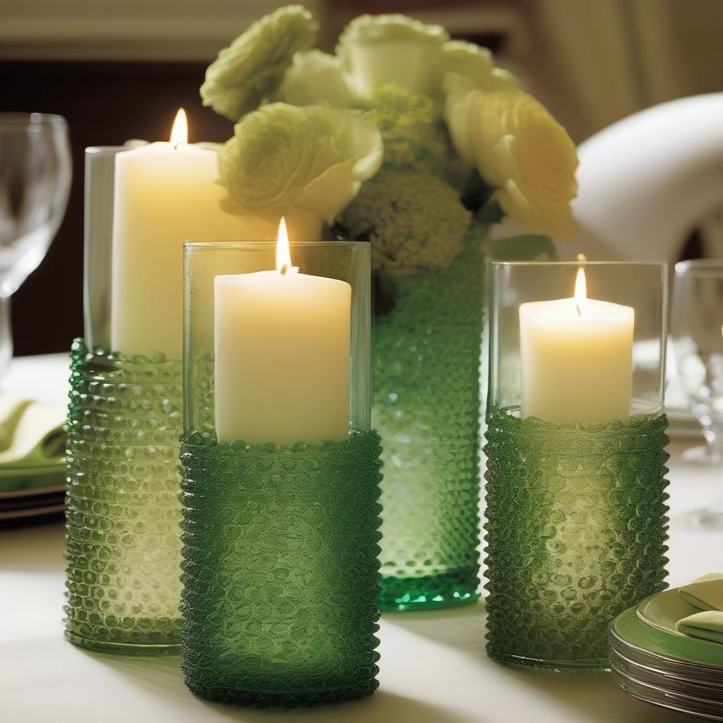 A dining table centerpiece featuring a collection of green hobnail glassware, including vases filled with flowers and candles in hobnail holders. 